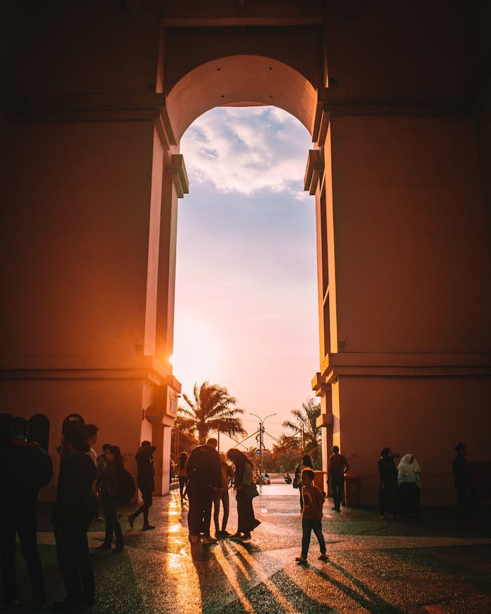 services-03 Silhouetted people gather under a grand arch at sunset with a stunning sky.