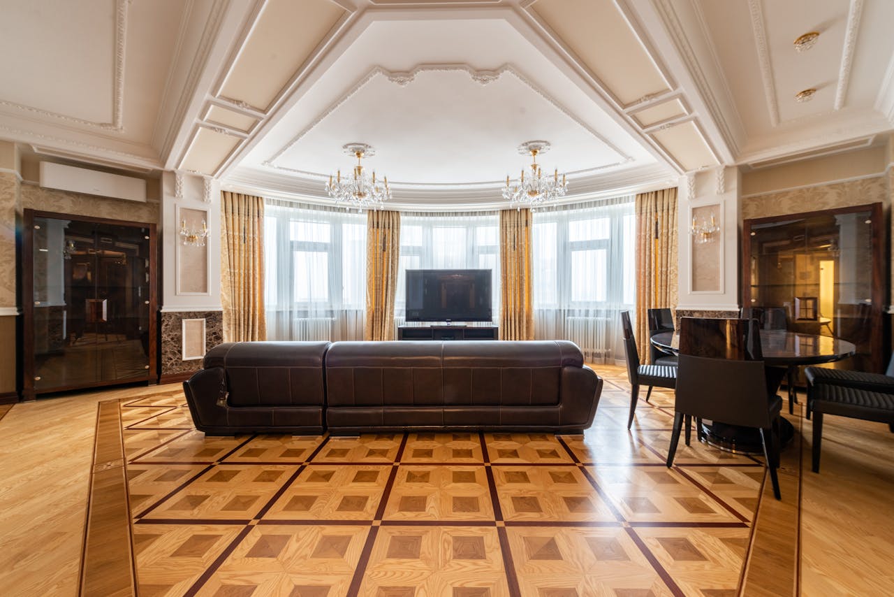 why-choose-us Spacious living room with a leather couch, large TV, and elegant decor, featuring chandeliers and parquet flooring.