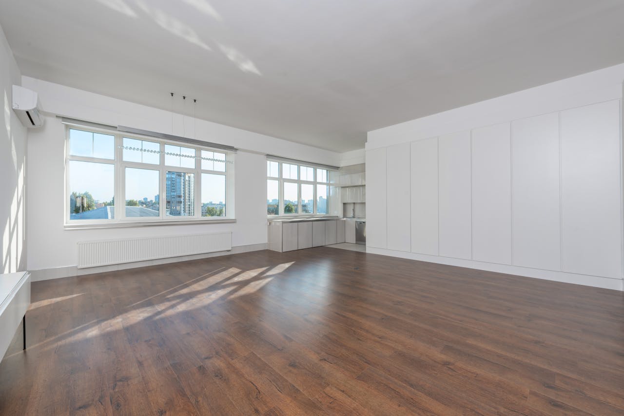 services-04 Bright and modern empty room with wooden floors and large windows, perfect for home design inspiration.