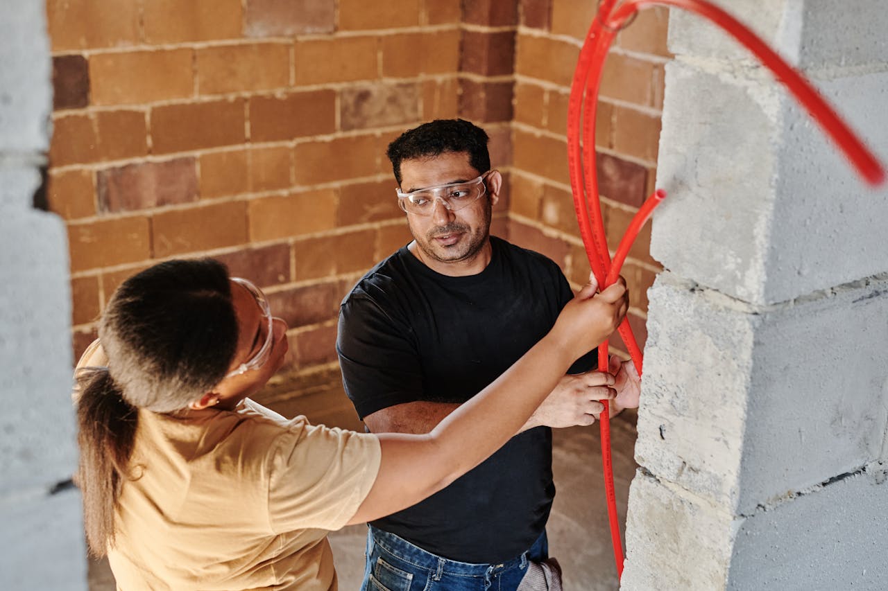 services-01 Two construction workers fitting red tubing on a brick wall at a construction site.